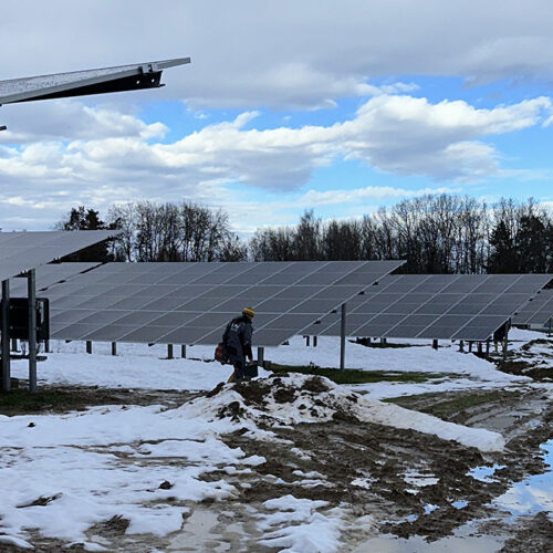 Eine Person in Winterkleidung betrachtet Solarmodule im schneebedeckten Solarpark.