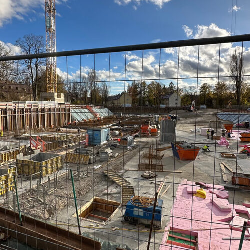 Baustelle mit Baugerüsten, Materialien in verschiedenen Farben, sonnig, wolkiger Himmel.