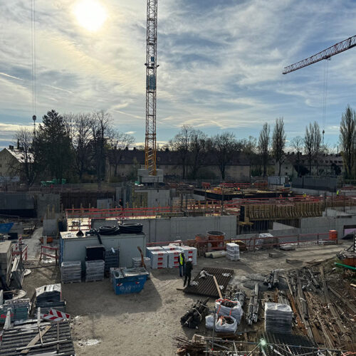 Baustelle mit Kränen, Baumaterialien und Arbeitern unter sonnigem Himmel.