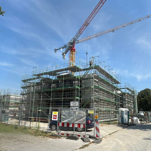 Eine Baustelle mit Gerüst, Kran und Straßensperren bei sonnigem Wetter.