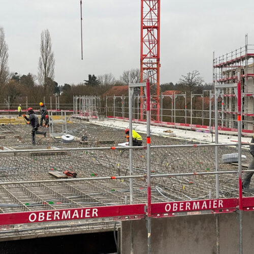 Bauarbeiter mit gelber Schutzkleidung arbeiten konzentriert an einem mehrstöckigen Gebäude.