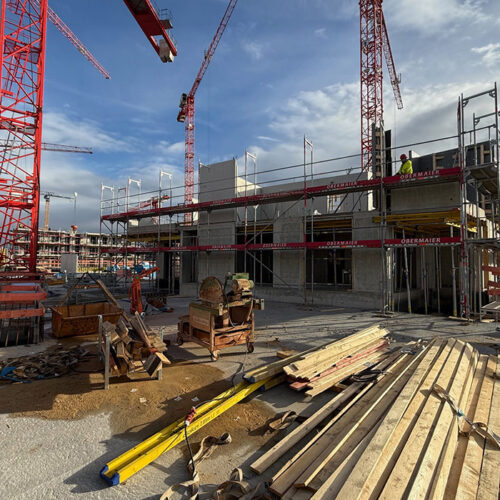 Eine Baustelle mit Baukränen, Gerüsten und Baumaterialien unter blauem Himmel.