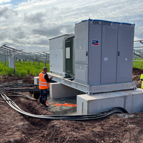 Zwei Personen in Sicherheitswesten arbeiten an einem Schaltkasten auf einer Solarfarm.